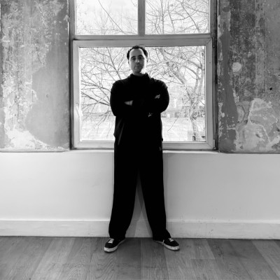 Bertan Kotil standing in front of a window, in black and white.